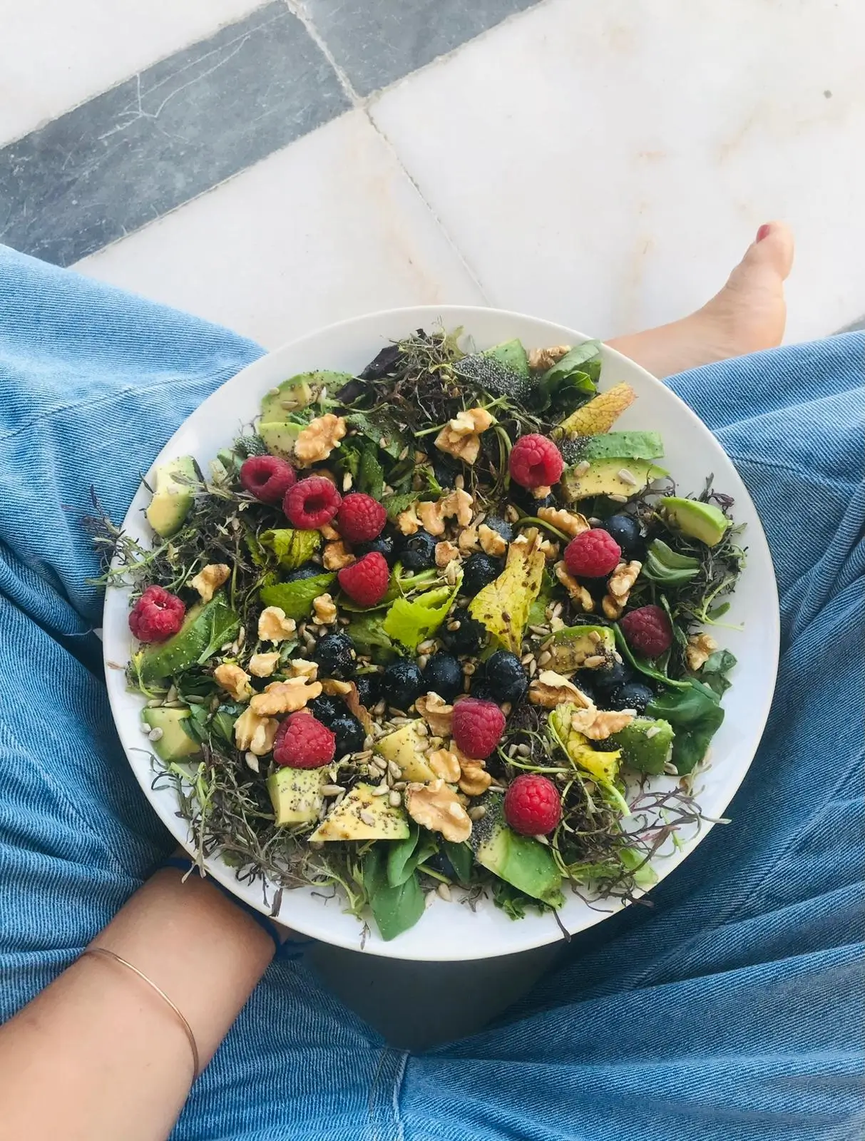 Salada de Alfaces Verdes com Abacate, Nozes, Framboesas e Mirtilos prato mão a segurar